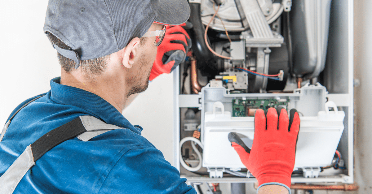 A Technician Wearing A Cap And Red Gloves Works On An Open Gas Furnace, Examining Its Internal Components.
