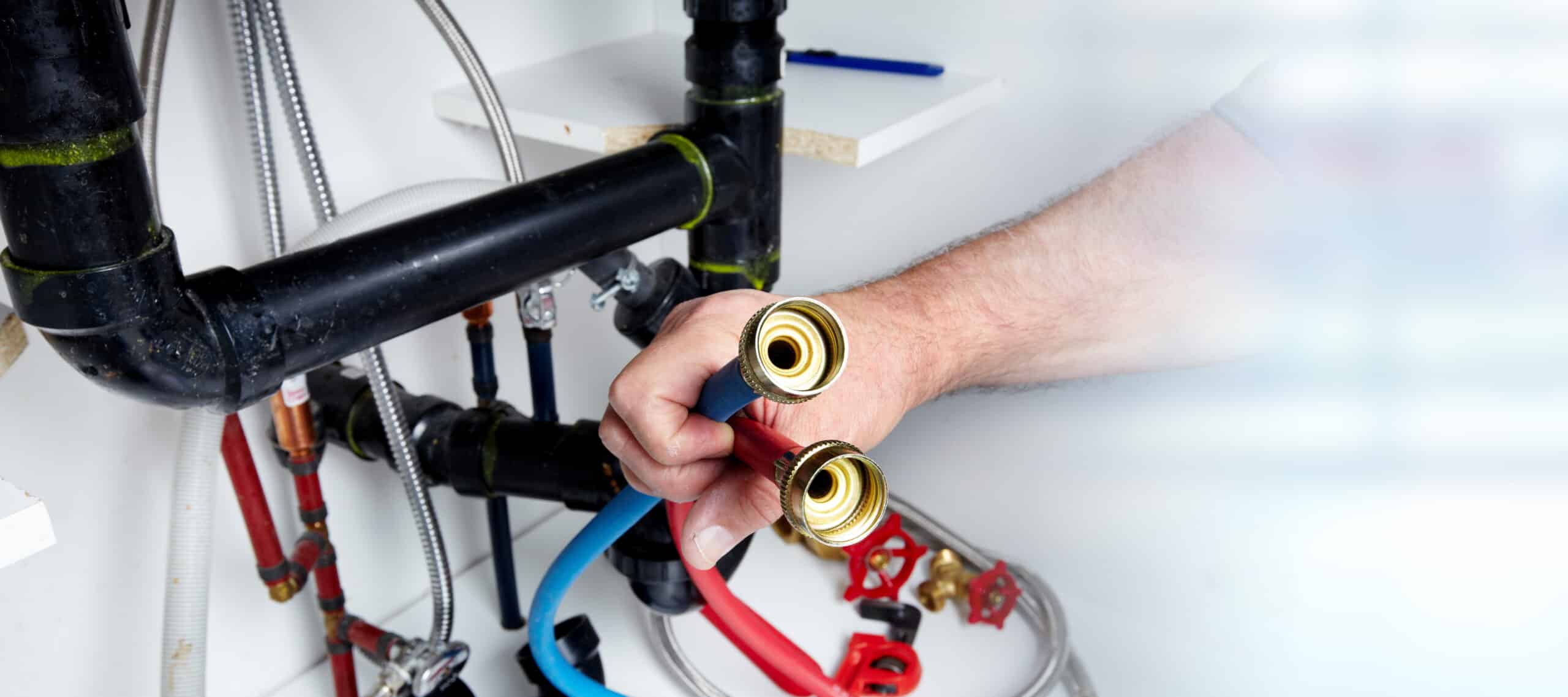 Person Holding Plumbing Hoses Near Pipes And Fittings.