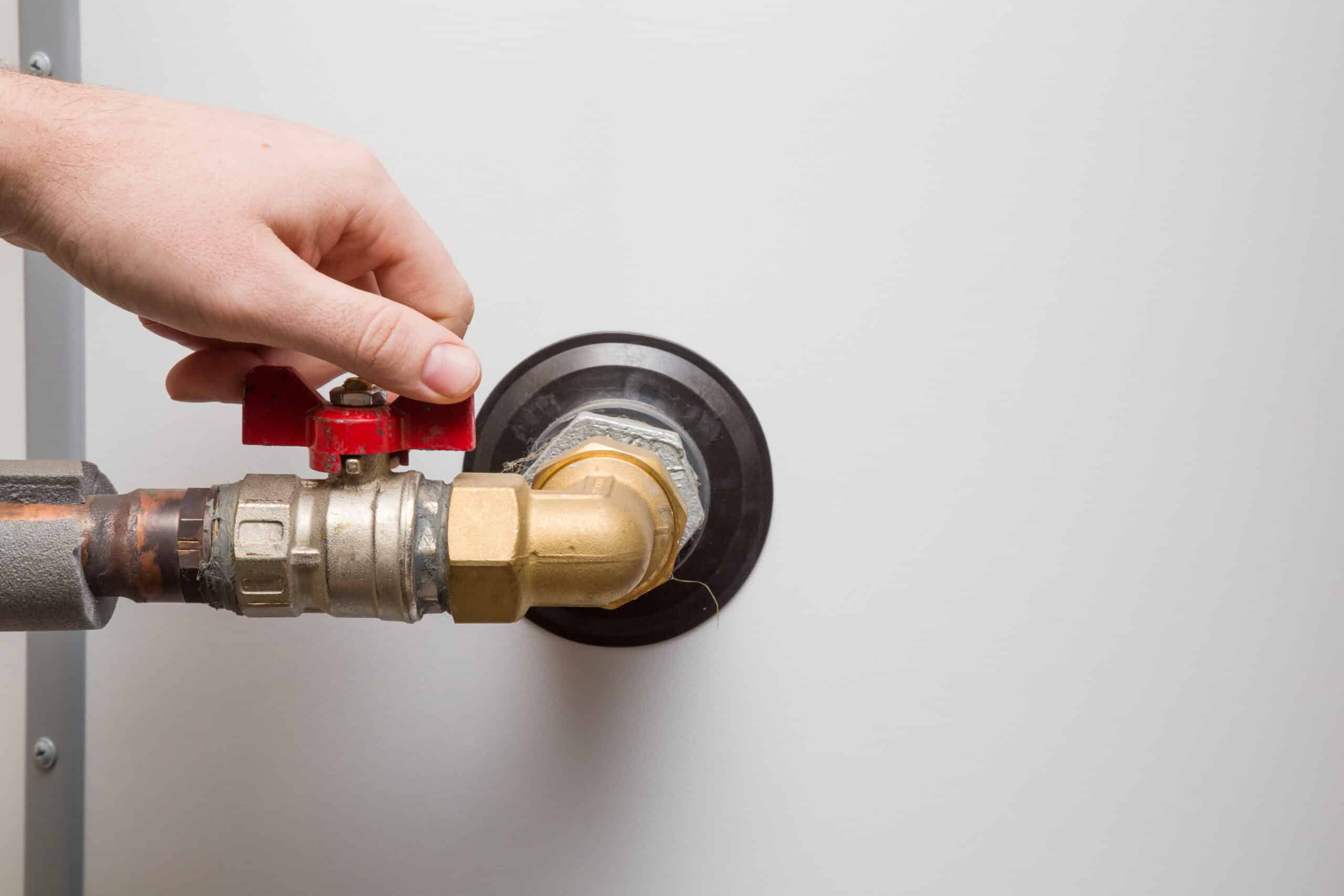 A Hand Turns A Red Valve On A Brass Pipe Connected To A White Wall, Adjusting The Flow.